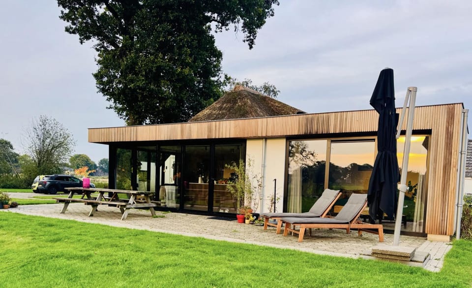 Het rieten boerderijtje in de avondzon, met weilanden eromheen